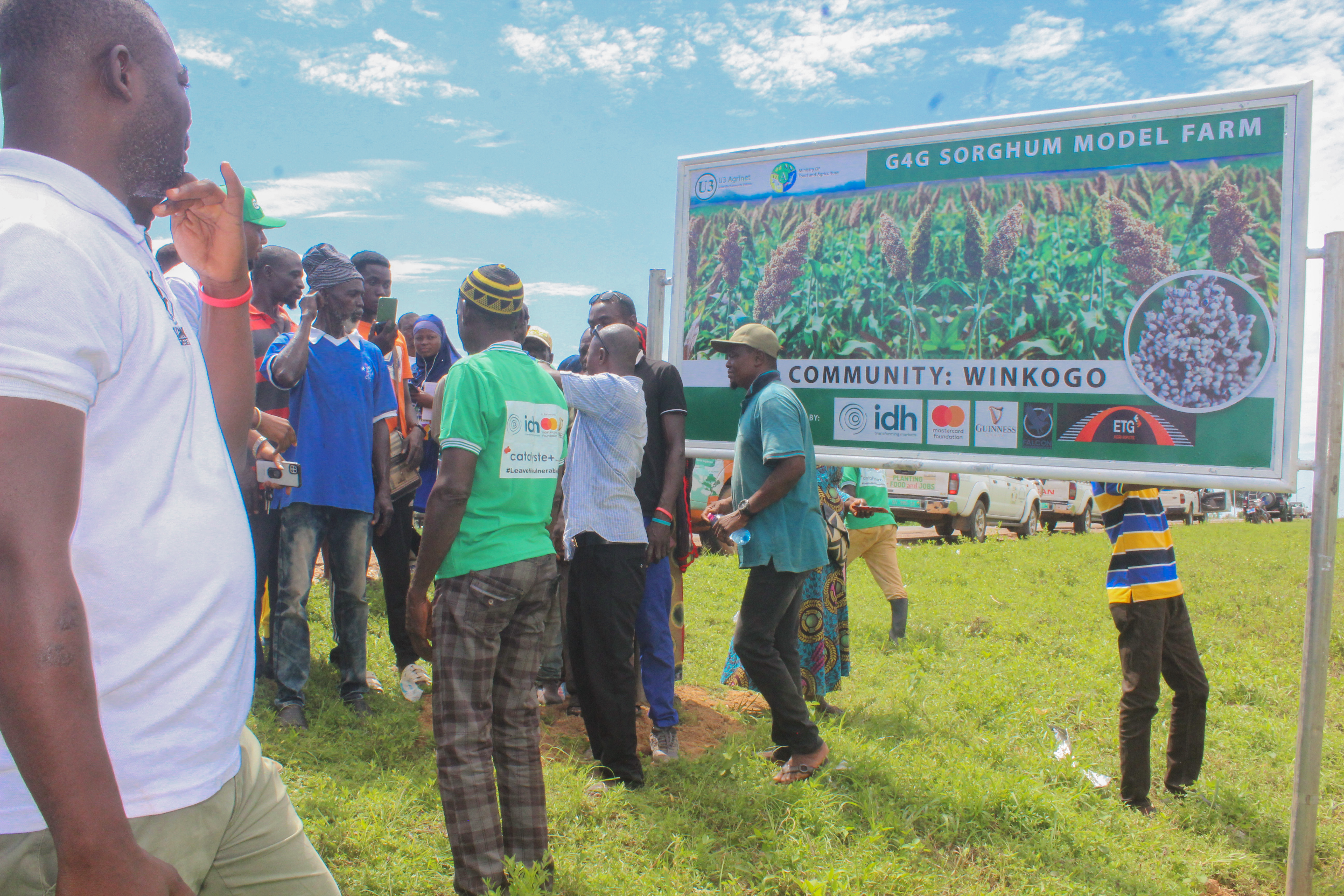 Farmers gathered at a project signboard during a field visit